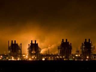 Towers of an industrial facility, with steam rising in the background.