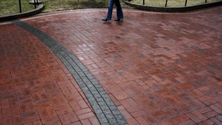 A view of patterned bricks, with the lower legs of a passerby in the background.