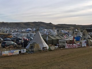 A cluster of tents, tipis, and parked vehicles in an open, treeless landscape.