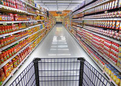 A photo taken at the end of of grocery store aisles, showing countless products displayed on the shelves. 
