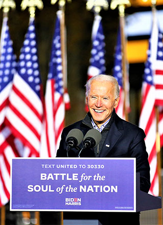 A smiling Joe Biden speaks from behind a podium with a sign reading “Battle for the Soul of the Nation”.