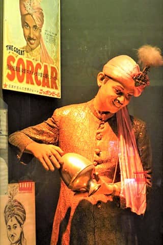A mannequin of a smiling gentleman in Indian garb, holding a golden lantern.