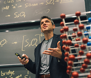 Professor Grossman standing in front of a blackboard with notes written on it at the front of the classroom.