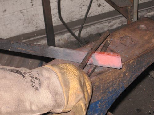 The two parallel arms of a spring fuller are applied to a glowing red bar.