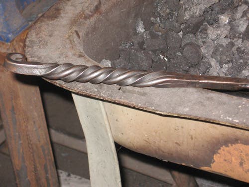 Two round and two square bars are forge welded together, twisted around each other, and scrolled at the end.