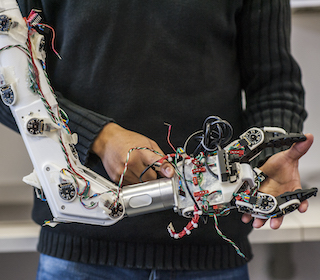 Image of someone standing behind a robotic arm with exposed wires.