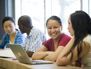 Two pairs of students sitting at a desk and discussing with each other.