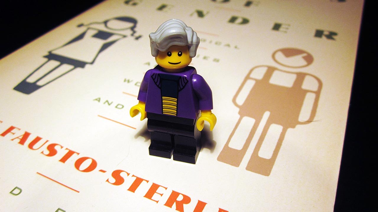 A small, plastic figure of a grey-haired woman stands upon the cover of a book.